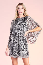 blonde model posing in the Ahri mixed animal boat neck caftan dress. The length is mini and the oversized sleeves hit around the elbow. The entire dress is printed with multiple animal prints, all in black and white fashion.  There is elastic lining the waist and sparkly metallic thread running throughout the piece